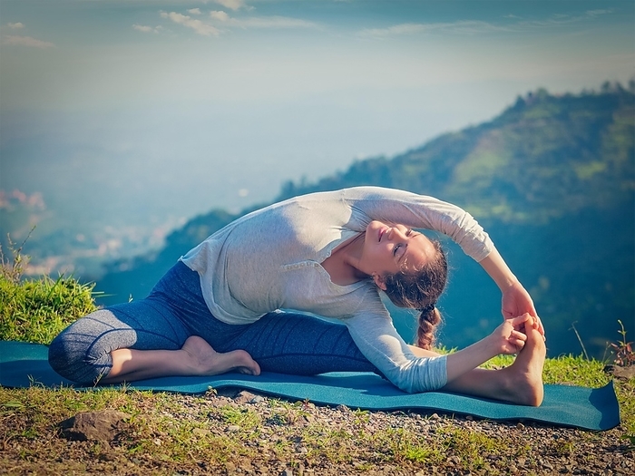 Yoga outdoors, young sporty fit woman doing Hatha Yoga asana parivritta janu sirsasana, Revolved Head-to-Knee Pose, in mountains in the morning. Vintage retro effect filtered hipster style image, Photo by Dmitry Rukhlenko
