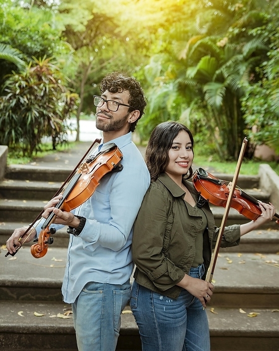Portrait of two young violists back to back outdoors. Portrait of smiling male and female violinist back to back outdoors. Two young violinists back to back holding their violins, Photo by Isai Hernandez