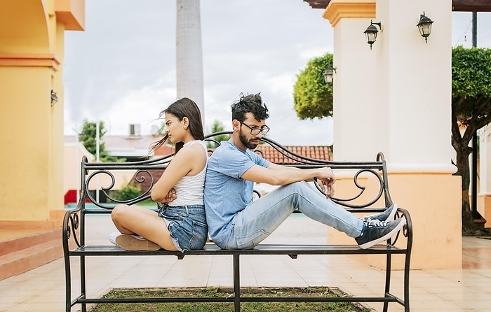 Upset couple sitting back to back on a park bench. Concept of a couple arguing in a park. Upset young couple sitting back to back outside, young couple arguing sitting back to back, Photo by Isai Hernandez
