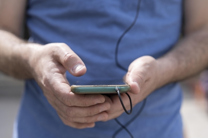 Close-up of a man's hands holding his phone with the headphones connected, Photo by Mariano Gaspar