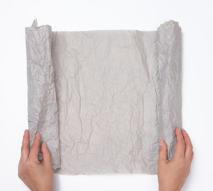 Two female hands hold an unwrapped roll of gray crumpled paper on a white background, top view Two female hands hold an unwrapped roll of gray crumpled paper on a white background, top view