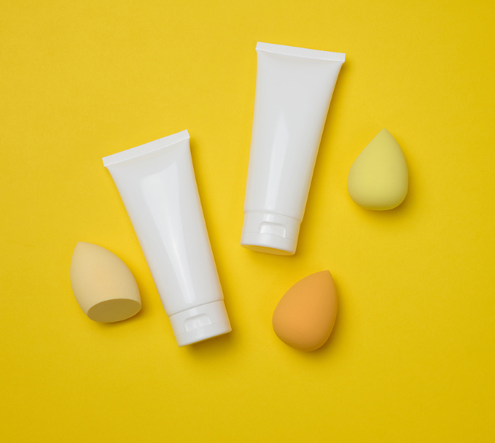 White plastic tubes for cream, gel and other cosmetics and sponges on a yellow background, top view White plastic tubes for cream, gel and other cosmetics and sponges on a yellow background, top view