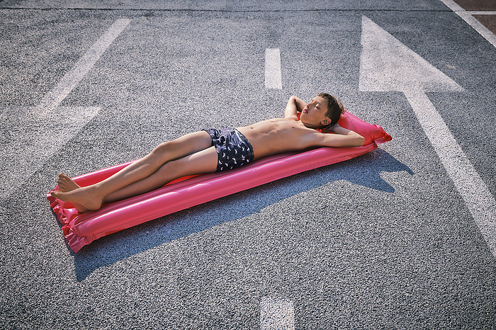 Shirtless boy lying on inflatable pool raft in parking lot