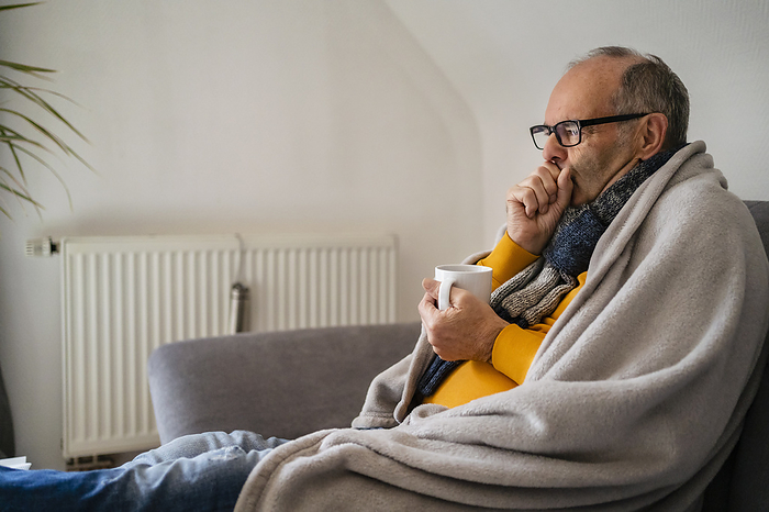Man holding mug feeling cold sitting on sofa at home