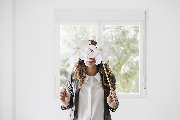 Young businesswoman covering eyes with white pinwheel toys