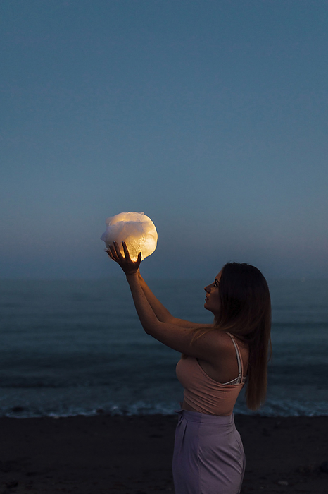 Young woman holding ball of cloth with light simulating moon at night