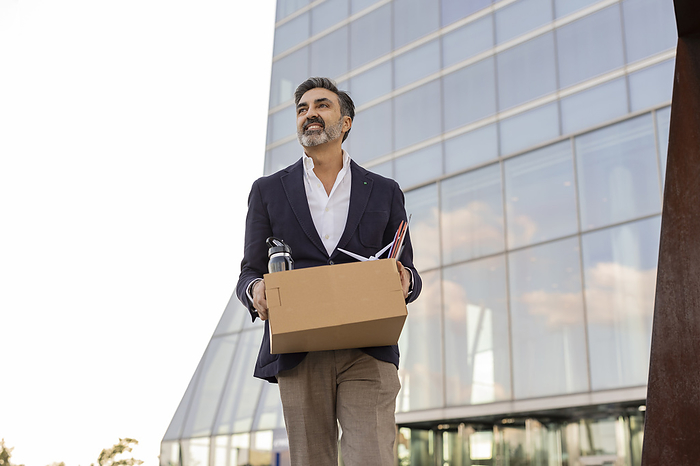 Smiling businessman leaving office with office supplies in box