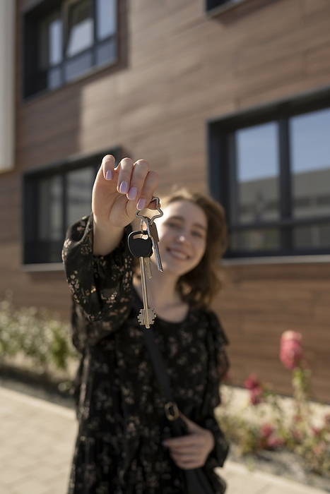 Young woman showing house keys standing in front of building