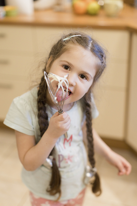 Portrait of little girl licking whipped cream off wire whisk