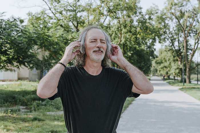 Smiling senior man wearing headphones enjoying music at park