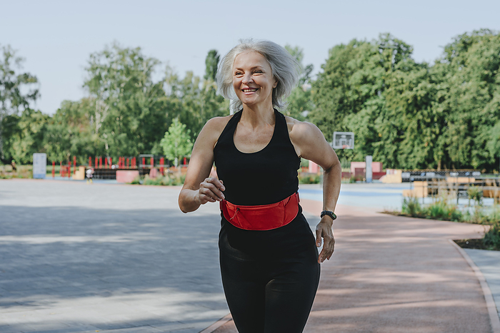 Happy mature woman with waistband jogging in park