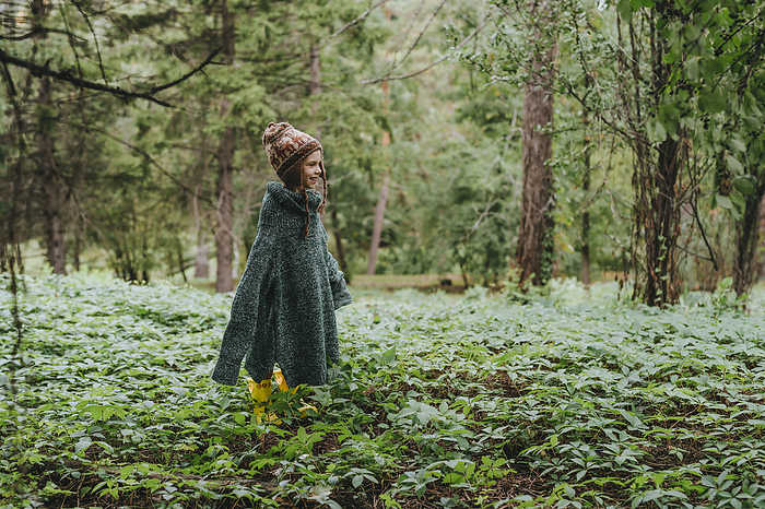 Girl wearing oversized sweater standing amidst plants in forest