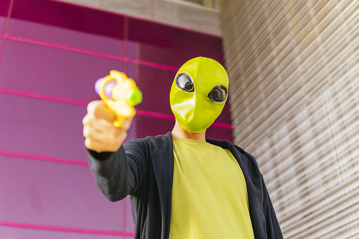 Man wearing alien mask playing with toy gun