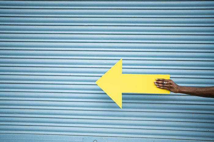 Hand of man holding yellow arrow sign in front of blue shutter