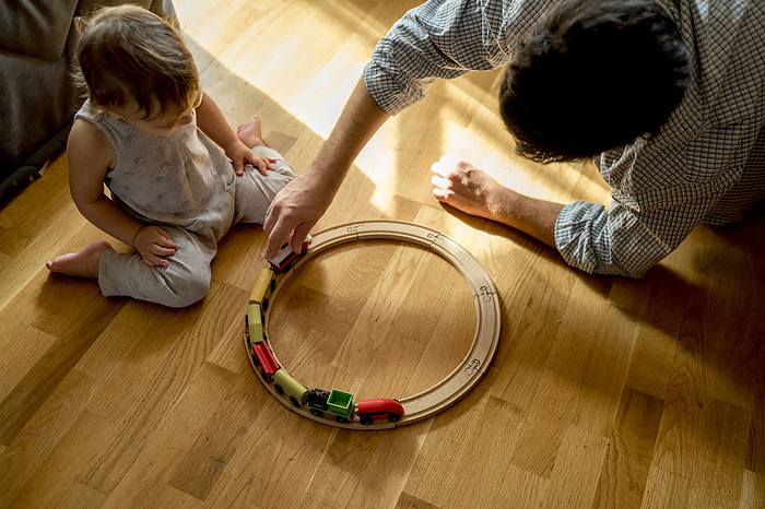 Father and son playing with toy train on hardwood floor at home