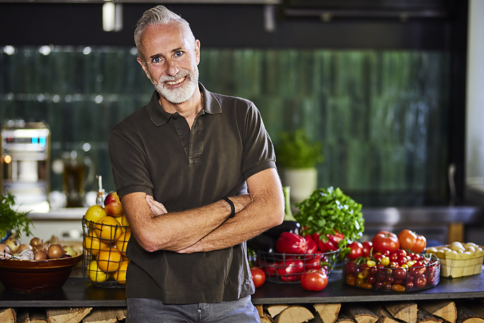 Happy man with arms crossed standing by kitchen counter