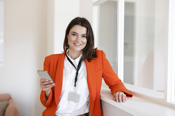 Happy businesswoman holding mobile phone in office