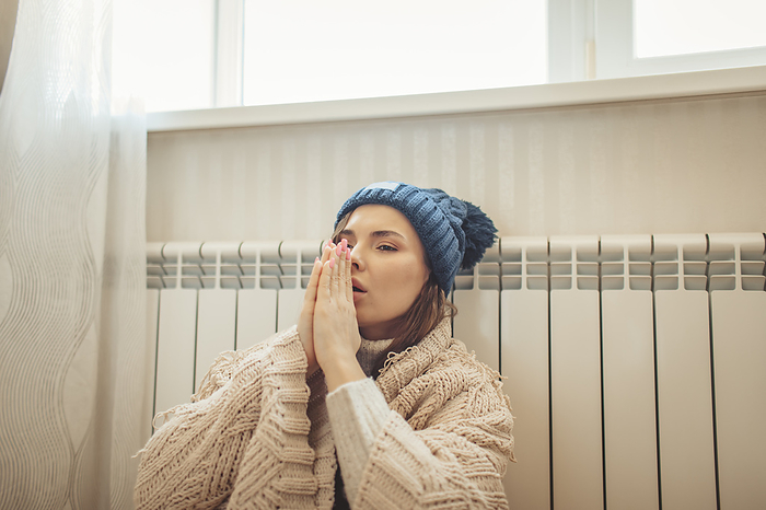 Woman wrapped in blanket rubbing hands leaning on radiator
