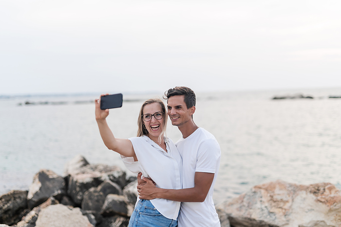 Happy couple taking selfie on mobile phone at beach