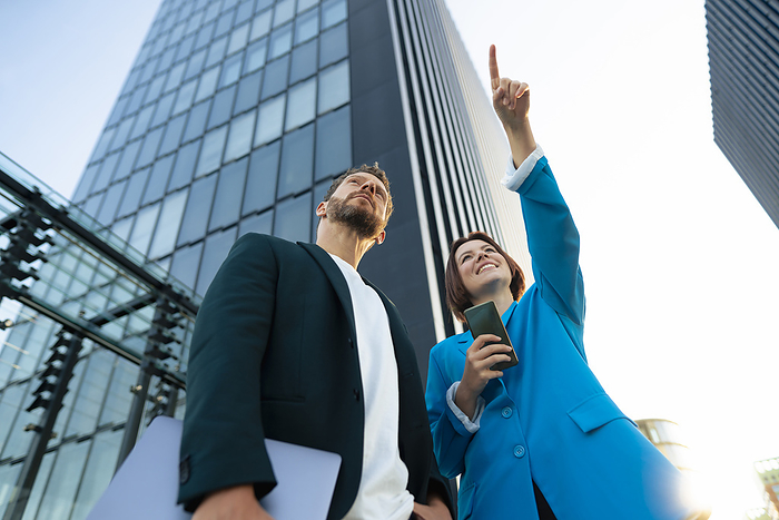 Businesswoman pointing to colleague standing near office building