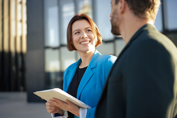 Smiling businesswoman with tablet PC looking at colleague on sunny day