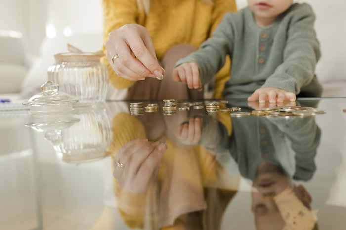 Young woman with son counting coins on table at home