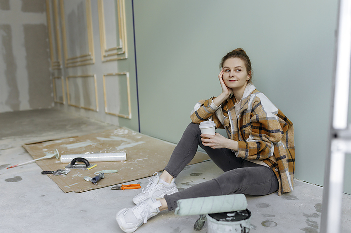 Thoughtful woman with disposable coffee cup sitting on floor at home