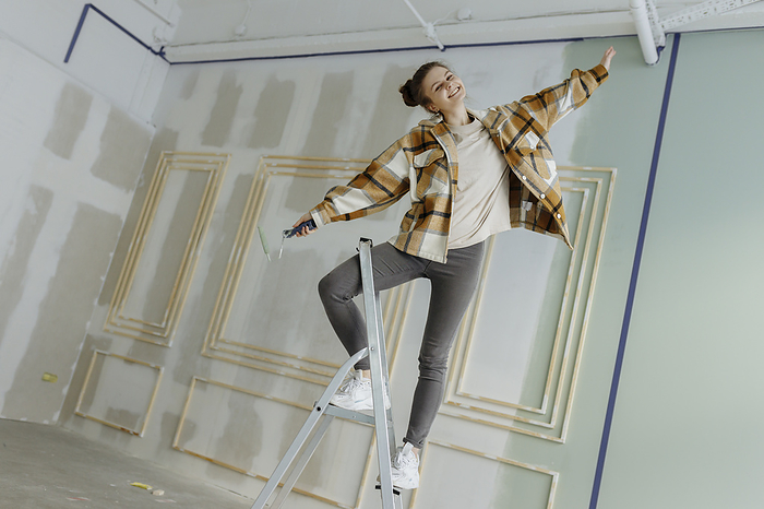 Happy woman dancing with arms outstretched on ladder at home