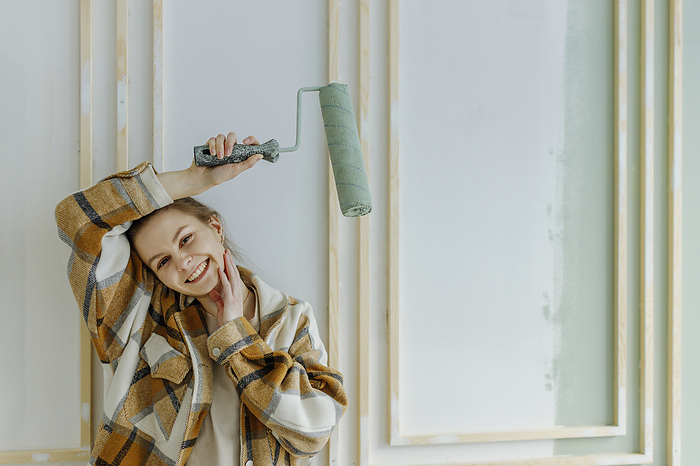 Smiling young woman holding paint roller over head at home