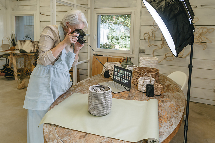 Craftswoman photographing crochet basket through camera on workbench in workshop