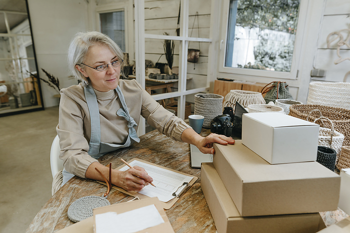 Mature craftswoman with clipboard analyzing box on workbench