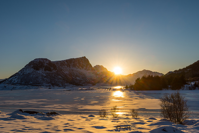 Sun setting behind snow clad mountains over frozen lake in dreamy winter landscape on the Lofoten islands in Norway on clear winter day Sun setting behind snow clad mountains over frozen lake in dreamy winter landscape on the Lofoten islands in Norway on clear winter day, Photo by Zoonar ROBERT RUIDL