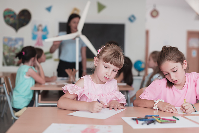 Little girls sitting in elementary school drawing on paper with their friends while sitting in a modern classroom, Photo by Zoonar/BENIS ARAPOVI