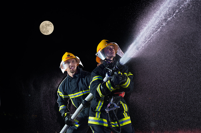 Firefighters using a water hose to eliminate a fire hazard. Team of female and male firemen in dangerous rescue mission. Firefighters using a water hose to eliminate a fire hazard. Team of female and male firemen in dangerous rescue mission., Photo by Zoonar benis arapovi