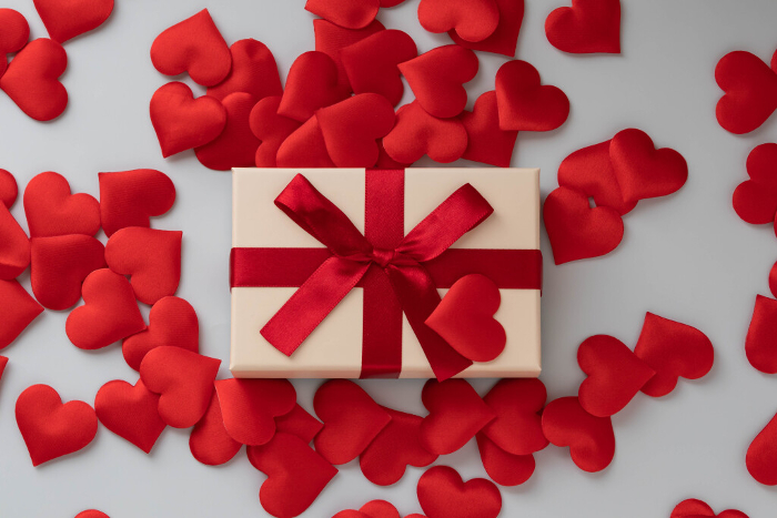 Image of sending and receiving love with red ribbon presents and hearts in a flat composition.
