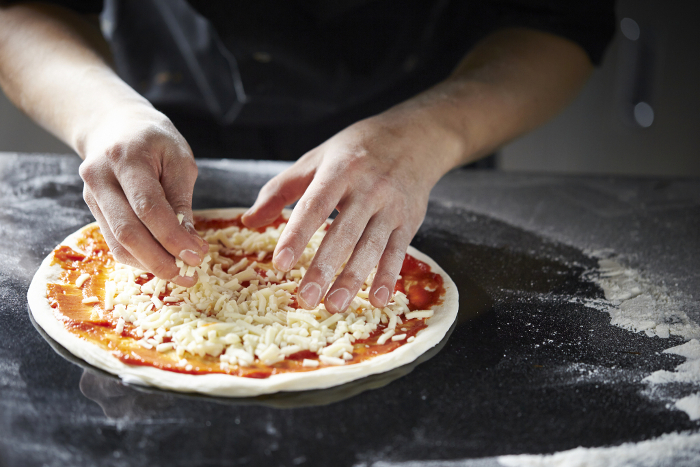 Man's hand putting cheese on pizza dough