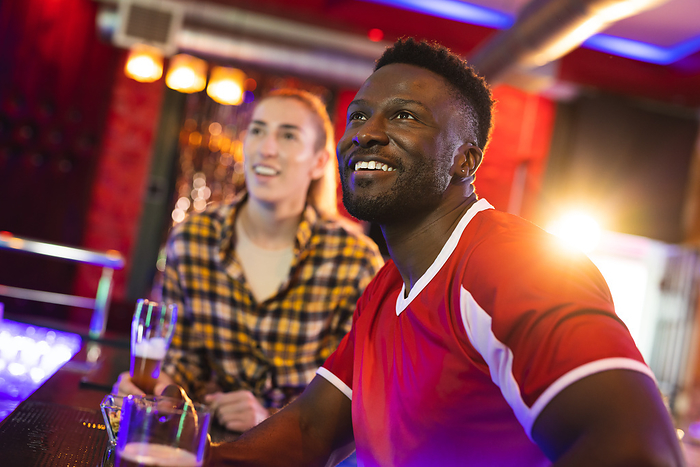 Diverse, excited male and female friend watching sports game showing at a bar. Friendship, fun, inclusivity, going out and socialising concept.