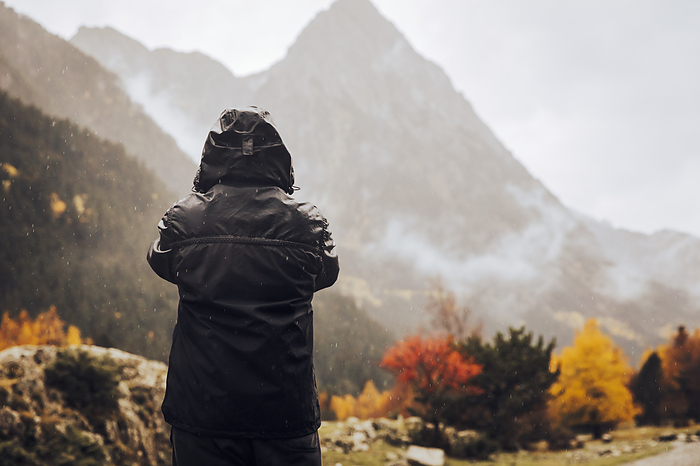 Boy in a raincoat taking photos of an autumn mountain landscape