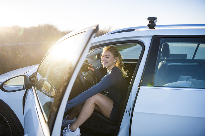 Young woman in tennis outfit getting out of car in sunny parking lot