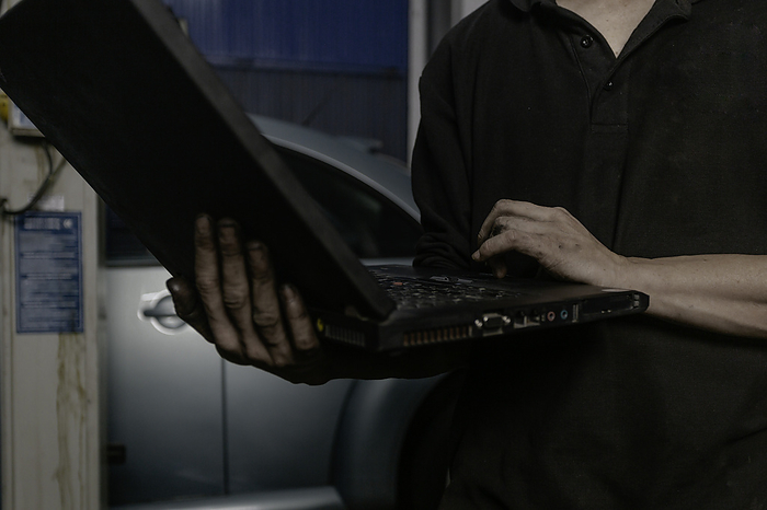 Car mechanic working on laptop in workshop