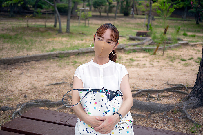 Kobe,Japan,A mature Japanese woman outdoors in a park, wearing a face mask, holding a bag. A mature Japanese woman outdoors in a park, wearing a face mask, holding a bag.