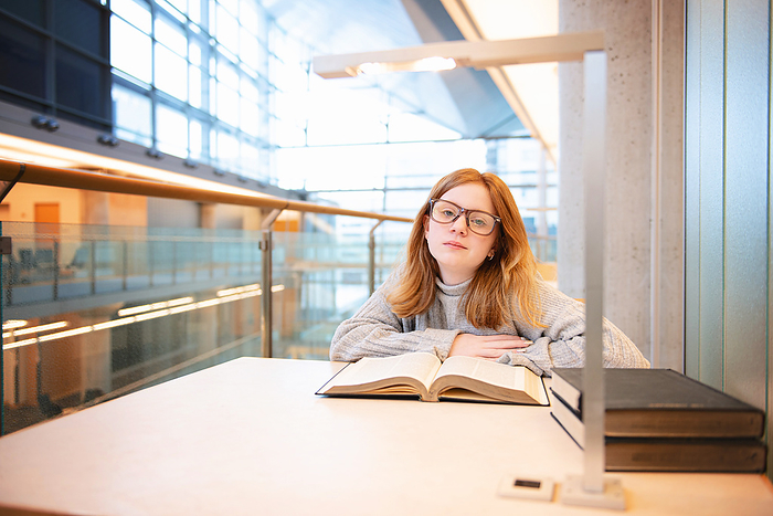 Teen girl with red hair and glasses reading at the library.