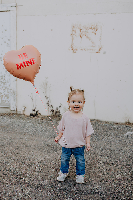 Happy toddler standing outside with heart valentines balloon