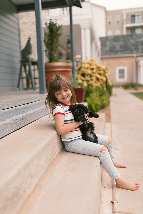 Small child sitting on steps holding a black puppy maltese outsi