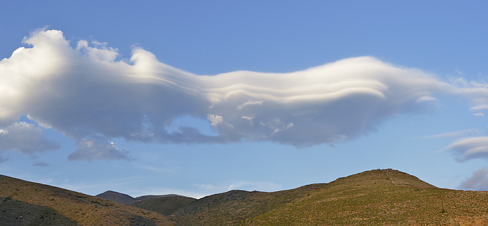 Lenticular cloud, Greece. Lenticular cloud, Greece. Lenticularis lentil shaped  from lenticula lentil  are stationary clouds that form mostly in the troposphere, typically in parallel alignment to the wind direction. They are often comparable in appearance to a lens or saucer. Nacreous clouds that form in the lower stratosphere sometimes have lenticular shapes. These lens shaped orographic wave clouds form when the air is stable and winds blow across hills and mountains from the same or similar direction at different heights through the troposphere., by DAVID PARKER SCIENCE PHOTO LIBRARY