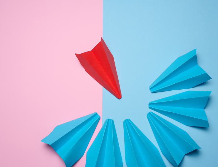A group of blue paper airplane surrounded one red boat, the concept of bullying, search for compromise. Top view A group of blue paper airplane surrounded one red boat, the concept of bullying, search for compromise. Top view