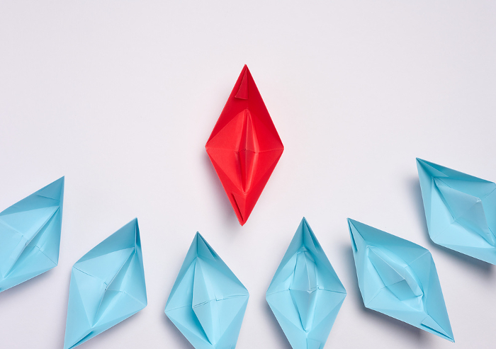 A group of blue paper boats surrounded one red boat, the concept of bullying, search for compromise. Top view A group of blue paper boats surrounded one red boat, the concept of bullying, search for compromise. Top view
