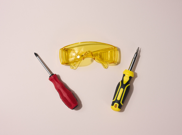 Transparent acrylic glasses and a screwdriver on a beige background, top view Transparent acrylic glasses and a screwdriver on a beige background, top view