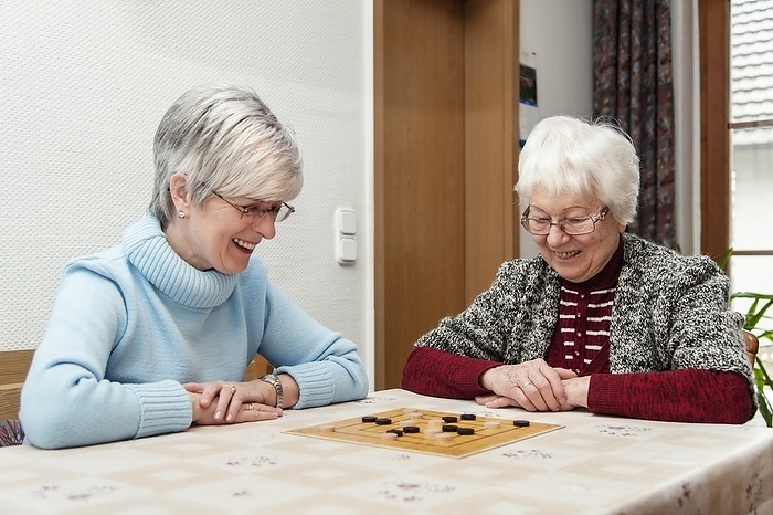 Two elderly women, senior citizens, mother and daughter, playing the board game 