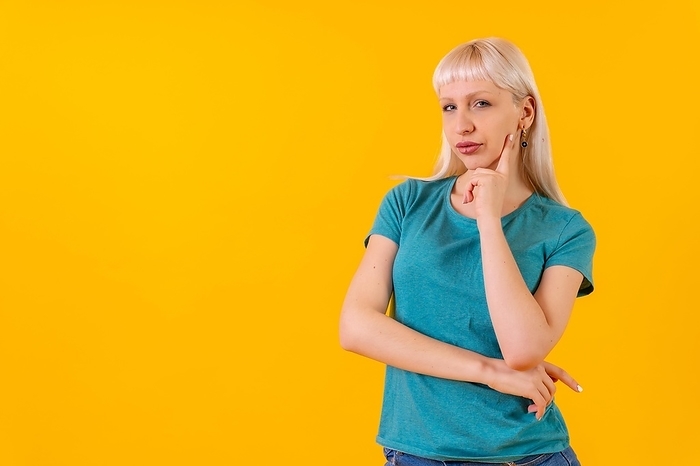 Portrait with pensive pose, copy space, blonde caucasian girl in studio on yellow background